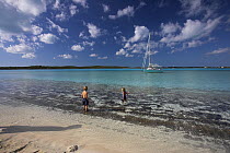 Children playing on the shore with a Shannon Shoalsailor moored beyond. This innovative, keelless, shallow draft beachboat is designed to roam shallow waters such as these in Exuma, the Bahamas.