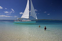 A Shannon Shoalsailor moored, with children in the sea wading out to it. This innovative, keelless, shallow draft beachboat is designed to roam shallow waters such as these in Exuma, the Bahamas.