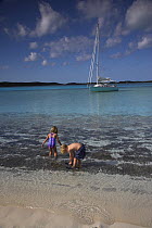 Children playing on the shoreline with a Shannon Shoalsailor moored beyond. This innovative, keelless, shallow draft beachboat is designed to roam shallow waters such as these in Exuma, the Bahamas.