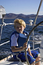 A little boy taking the wheel on cruising yacht, Mexico.