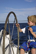 Little boy taking the wheel and eating a biscuit on a cruising yacht, Mexico.