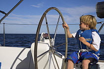 A little boy taking the wheel and eating a biscuit on a cruising yacht, Mexico.