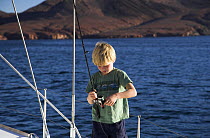 A young boy preparing his fishing rod on the deck of a sailboat, Caleta dela Isla, Mexico. Model released.
