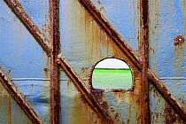 Bright green sea through a hole in a rusty blue boat hull. Ireland, Europe.