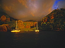 Dramatic clouds over catamarans anchored at sunset in the Bay of Virgins, Marquesas Islands, French Polynesia.