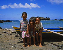 Polynesian children beside a traditional boat, smiling for the camera in the Marquesas Islands, French Polynesia.