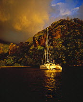 Dramatic clouds over an anchored catamaran at sunset in the Bay of Virgins, Marquesas Islands, French Polynesia.