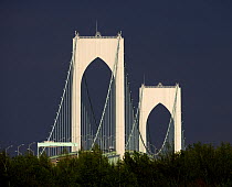 View from Jamestown of the arches of Newport Bridge lit up by the sun and set against the dark sky, Rhode Island, USA.