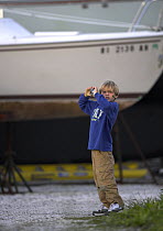 A young boy taking a photograph at a marina in Jamestown, Rhode Island, USA.