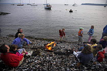 Families sitting round a fire on a stony beach, Newport, Rhode Island, USA.