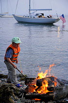 Young boy on a stony beach poking a fire with a stick, Newport, Rhode Island, USA. Model and Property Released.