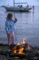 Young girl on a stony beach poking a fire with a stick, Newport, Rhode Island, USA. Model and Property Released.