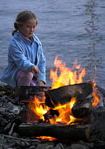 Young girl on a stony beach poking a fire with a stick, Newport, Rhode Island, USA.