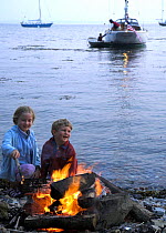 Two children on a stony beach beside a fire, Newport, Rhode Island, USA.