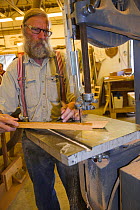 Man sawing a piece of wood for boat construction.