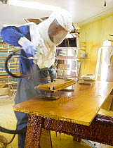 Man wearing protective mask, spray varnishing a small interior piece during yacht construction.