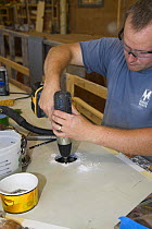 Man drilling a hole in an interior boat part during construction.