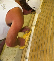 Man planing the rail of the deck on a yacht under construction.