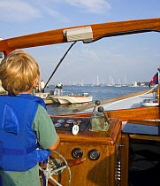 Young boy in lifejacket at the helm of a small cruising motorboat.