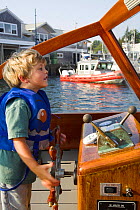 Young boy in lifejacket at the helm of a small cruising motorboat. Model released.
