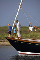 Young family anchored aboard a cruising yacht, with small boy swinging from the sheets. Rhode Island. Model released.