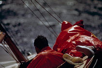 Crew lie along the deck of "Dragon", hiking out in old-fashioned oilskin waterproofs.
