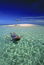 Young girl in bikini floating in shallow water just off an idylic sand island in Fiji. Model released.