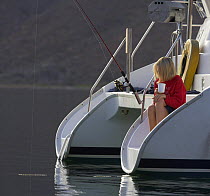 A girl with a drink watching the fishing pole on the stern of a cruising catamaran in Caleta Partida, Mexico. 2006.