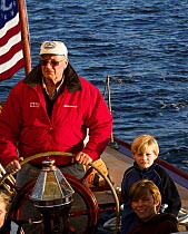 A man at the helm during an evening charter onboard 12m yacht "Gleam" sailing in Narragansett Bay off Newport, Rhode Island, USA. September 2006.