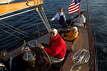 Helmsman and passengers during an evening charter onboard 12m classic yacht "Gleam" sailing in Narragansett Bay off Newport, Rhode Island, USA, 2006.