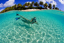 Split-level view of a woman snorkeling with a camera off a tropical beach, British Virgin Islands, Caribbean, December, 2006. Model Released.