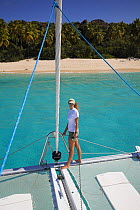 Woman standing on the deck of a catamaran in front of a tropical beach, British Virgin Islands, Caribbean, December, 2006.