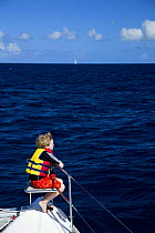 Young boy sitting in bow seat on the deck of a catamaran looking out to sea, British Virgin Islands, Caribbean. December 2006.