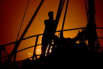 Fisherman on a trawler, watching an oil rig flaring off gas at night in the North Sea. September 2006.