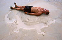 Simon King lying beside sand imprint of Saltwater crocodile while on location filming for BBC Blue Planet series, 2002,  Crab Is. Queensland, Australia